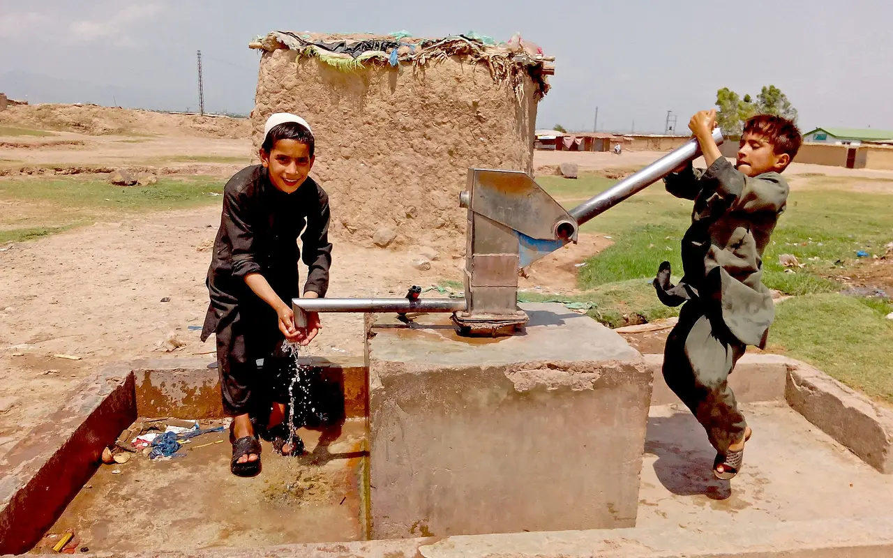 Two Afghan boys pumping water from a hand pump at a refugee settlement near Islamabad