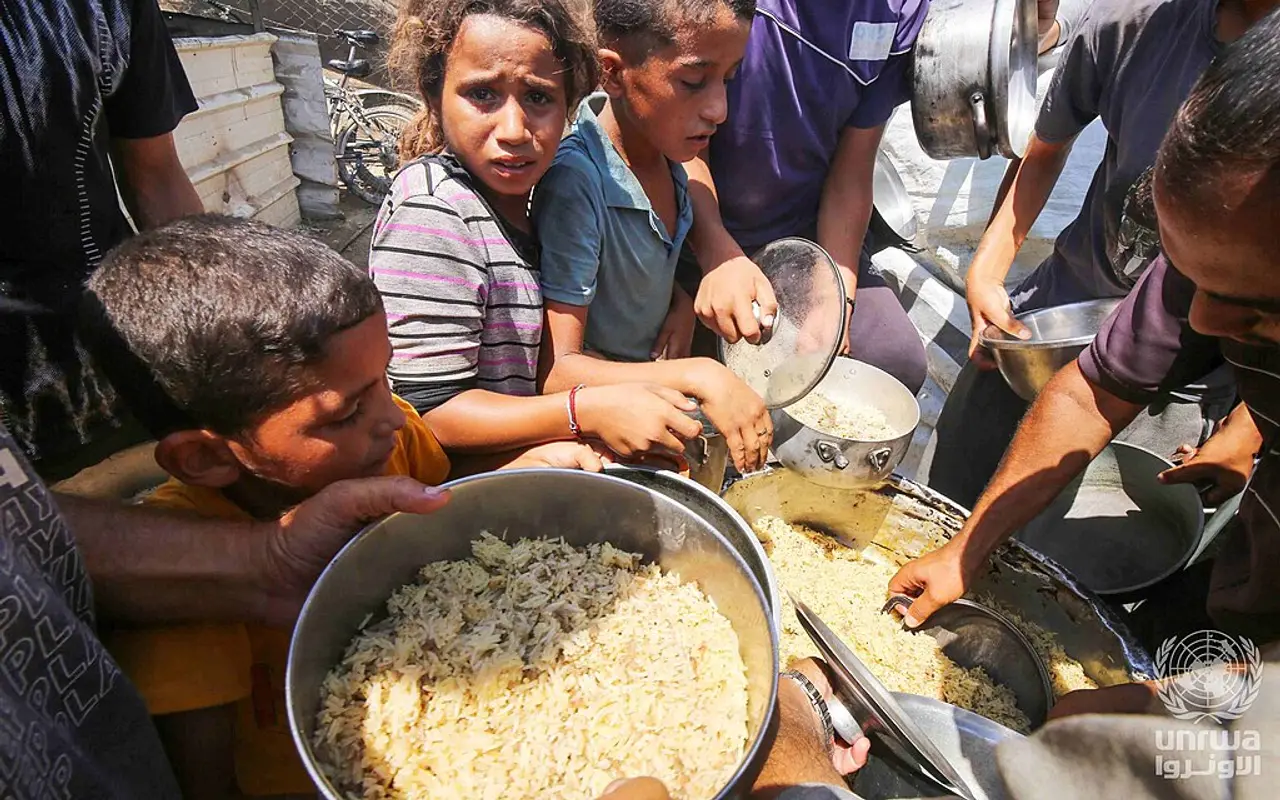 Displaced Palestinians holding pots as they line up for cooked food in Deir el-Balah, Gaza