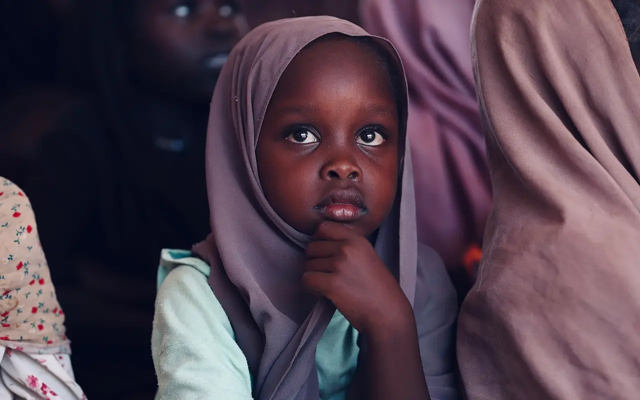 A young girl in a headscarf looking at the camera in a camp for displaced people in Sudan