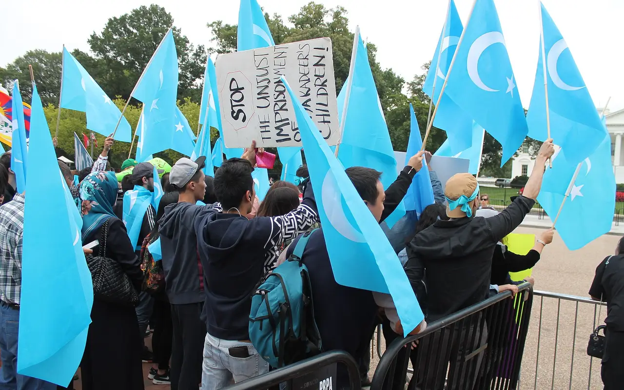 Demonstrators holding blue flags and a sign reading 'Stop the unjust imprisonment' at a Uyghur rights protest in Washington, DC